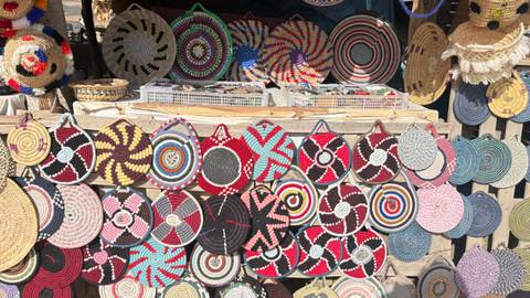 Sunlit market stall displaying rows of colourful woven basket lids and trays in geometric patterns.