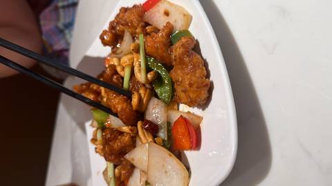 Close-up of a stir-fried chicken and vegetable dish with cashews being picked up by chopsticks.