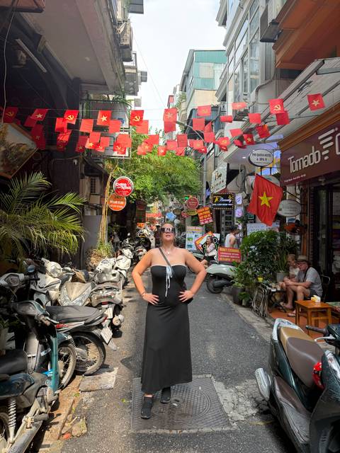 Tourist poses confidently beneath strings of Vietnamese flags in Hanoi’s bustling Old Quarter alley.