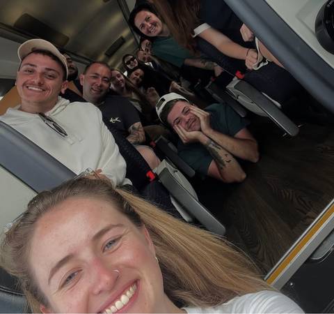 Playful selfie of a group of young travellers seated inside a tour bus.
