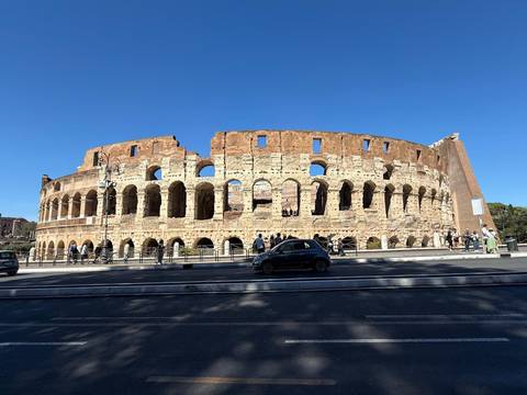 Wide street-level view of the Colosseum in Rome under bright blue sky.