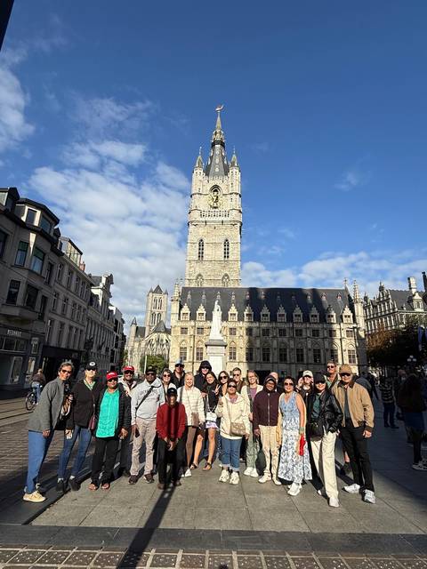 Large tour group posing in front of Belfry of Ghent on a sunny day.