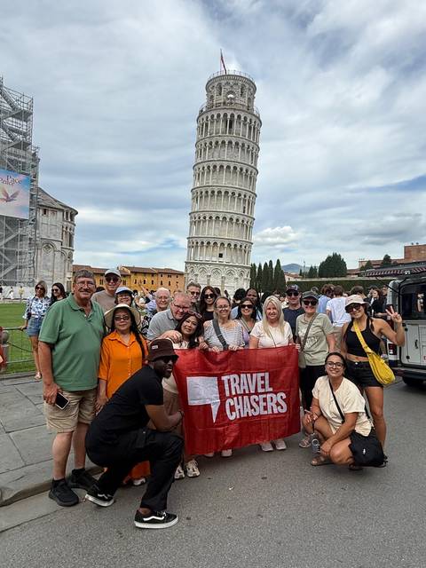 Tour group holding banner in front of the Leaning Tower of Pisa.