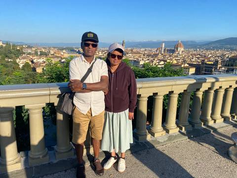 A couple stands at a scenic terrace overlooking Florence with the iconic Duomo and cityscape spread out beneath a clear blue sky.