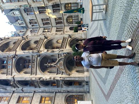 Two travellers pose in a grand neo-gothic courtyard with ornate arches and statues in a European city.