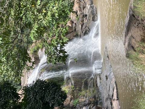 Multi-tiered jungle waterfall cascades into a brownish pool surrounded by lush foliage.