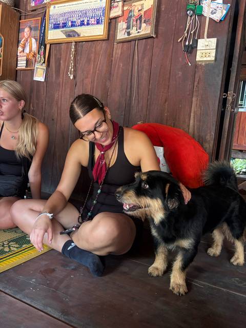 Traveler smiles while petting a friendly black dog inside a rustic wooden hut.