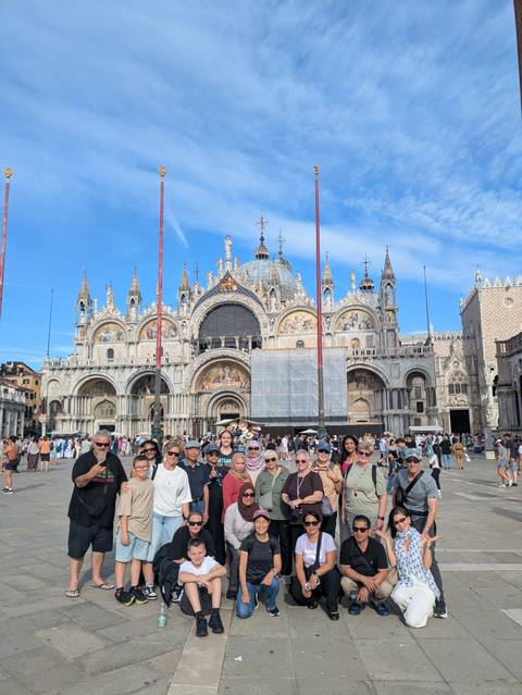 Tour group poses in front of St. Mark's Basilica on a bright day in Venice's St. Mark's Square.