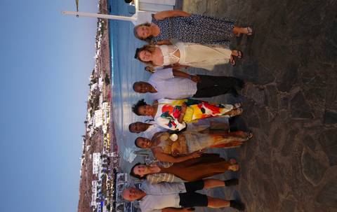 Group of friends dressed for an evening out pose beside the waterfront of Mykonos as lights twinkle in the distance.