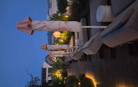 Stylish rooftop lounge with lined sunbeds and soft lighting overlooking Athens at dusk.
