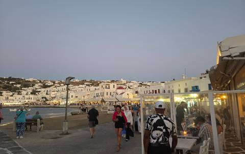 Evening crowds wander the harborfront street lined with whitewashed Mykonos buildings and cafés.