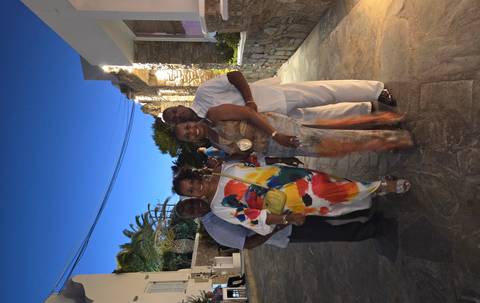 Four well-dressed friends pose on a cobbled lane under the evening sky in Mykonos.