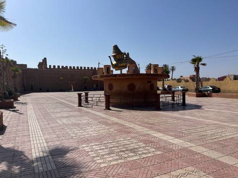 Open square with a giant teapot sculpture and fortress walls in the background on a sunny day.