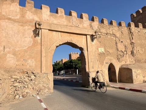 Cyclist passes through an ancient adobe archway with crenellations and textured stonework.
