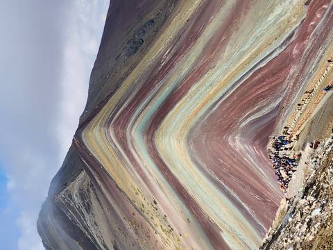 Striking multicoloured strata of Rainbow Mountain with a line of trekkers ascending the ridge.