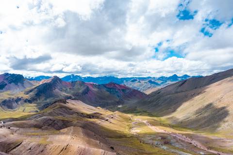 Wide Andean valley with rainbow-tinged hills, glaciers on horizon and dynamic cloud shadows.