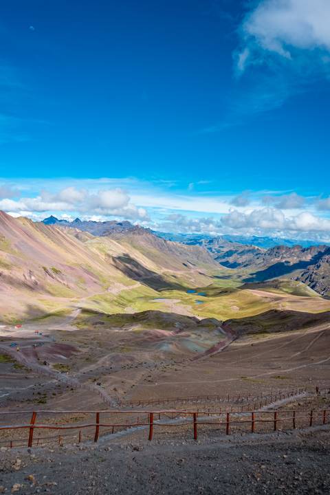 High-altitude panorama with emerald ponds and pastel mountains under bright blue sky.