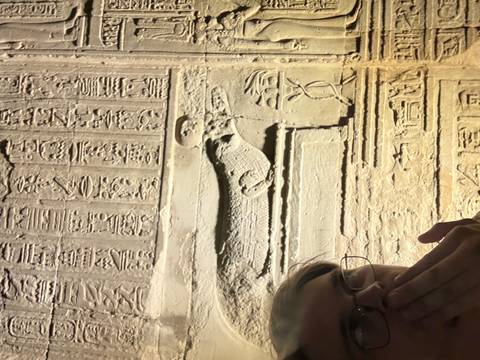 Close-up selfie beside illuminated ancient Egyptian hieroglyphic wall relief showing a crocodile figure.