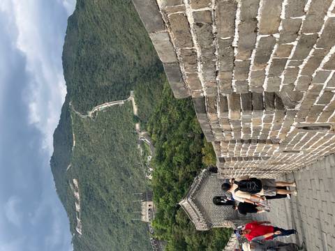 Visitors walking along the Great Wall of China with lush green mountains stretching behind.