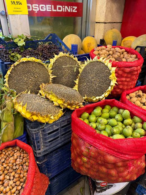 Colourful market display of giant dried sunflower heads, fresh corn and green plums.