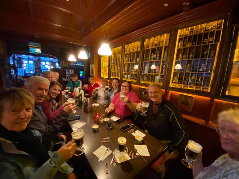 Lively pub interior where travellers raise glasses of Irish coffee around a long wooden table.