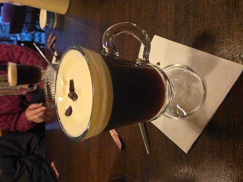 Close-up of creamy Irish coffee garnished with coffee beans in a glass mug on a wooden table.