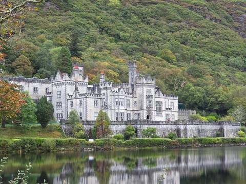 Majestic grey stone Kylemore Abbey reflected in a calm lake backed by forested hillside.