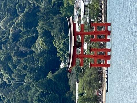 Iconic red torii gate of Itsukushima Shrine rises from the blue sea against a forested mountain backdrop.