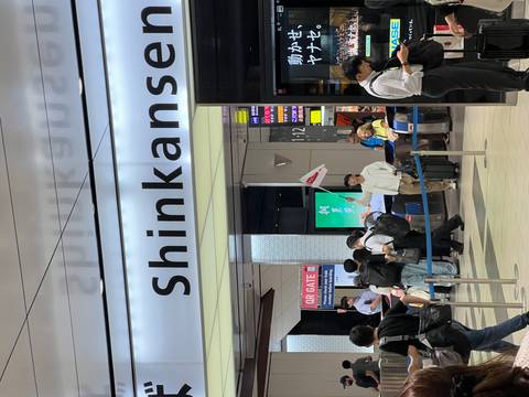 Busy Shinkansen station entrance with travellers queuing beneath a large sign.