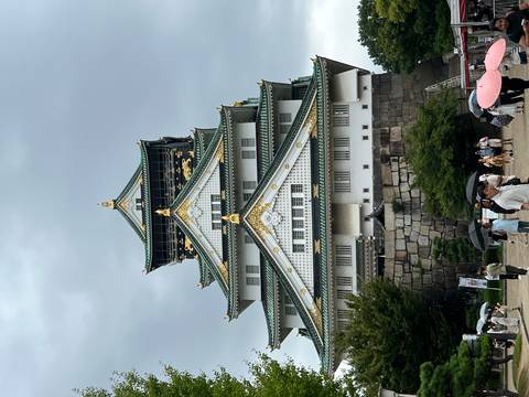 Impressive white and green Osaka Castle towers above visitors carrying umbrellas on an overcast day.