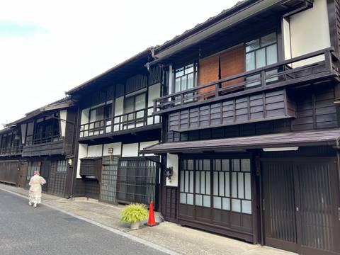 Row of preserved dark-wood machiya townhouses along a quiet street with a kimono-clad walker.