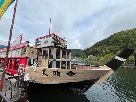 Traditional wooden pleasure boat with bold red accents moored on a lake backed by forested hills.