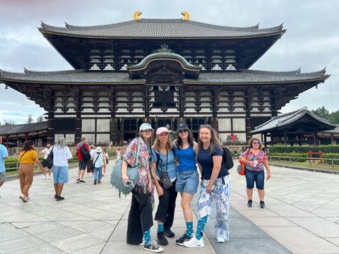 Friends pose happily in front of the grand wooden facade of Todai-ji temple while visitors mill about.