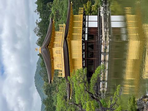 The iconic gold-leaf covered Kinkaku-ji temple reflected in a tranquil pond with forested hills in the background.