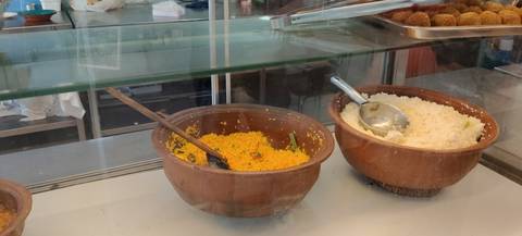 Two clay pots of yellow and white rice behind a glass counter inside a casual eatery.