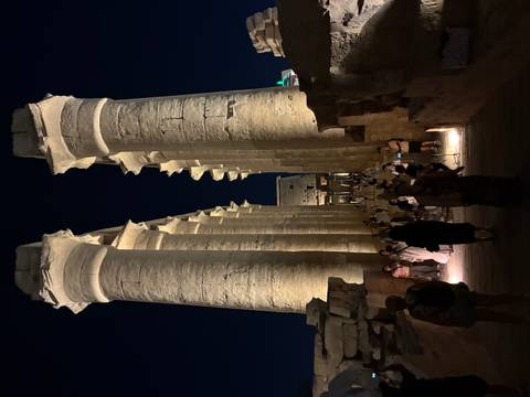 Night view of the illuminated colonnade of Luxor Temple with visitors walking between towering columns
