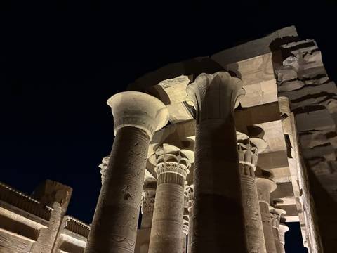 Up-lit sandstone columns with lotus capitals of an ancient Egyptian temple set against a dark sky
