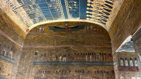 Richly painted tomb chamber with star-studded blue ceiling and winged sun disk motif above hieroglyphs