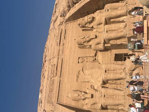 The colossal statues of Ramses II at Abu Simbel Temple bathed in bright sunlight with tourists below
