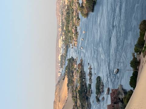 Vertical shot of the Nile River coursing between sandy hills and green islands under clear skies