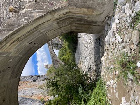 Stone arch bridge framed beneath a modern concrete span over a dry, rocky riverbed in Epirus mountains