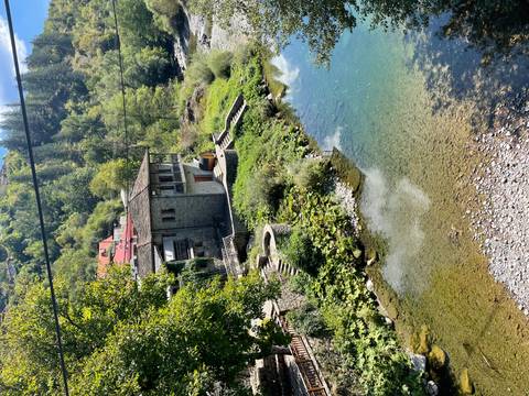 Traditional stone house with red roof beside a clear blue stream in a leafy Greek valley