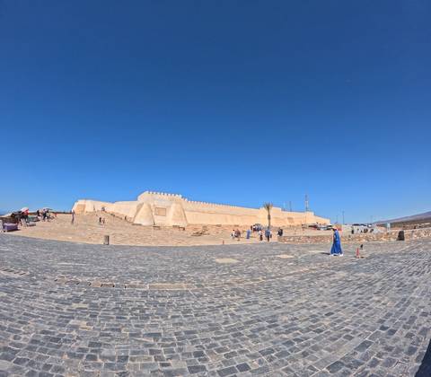 Panoramic view of a long, sand-coloured kasbah wall against a deep blue sky in southern Morocco