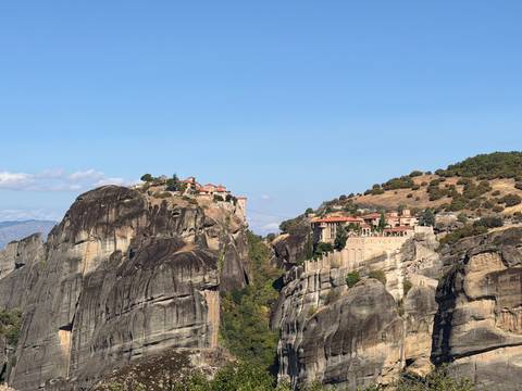 Dramatic monasteries perched atop towering rocky pillars under a clear blue sky.