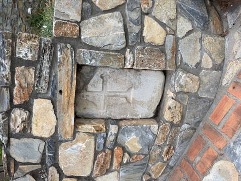 Weathered stone relief with a cross set into a rustic rock wall.