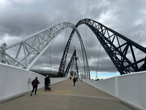 Matagarup Bridge in Perth with dramatic white and black arches spans the Swan River beneath moody clouds and pedestrians.