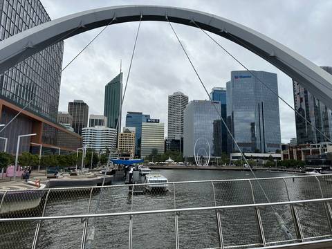 Modern skyline of Perth seen across Elizabeth Quay with boats and curved pedestrian bridge framing the view.