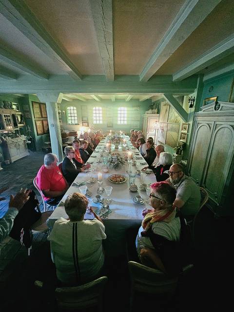 Long banquet table set for tea in an elegant historic room with a large tour group seated.