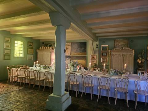 Elegant dining room with long table set with candles and vintage chairs beneath wooden beams.