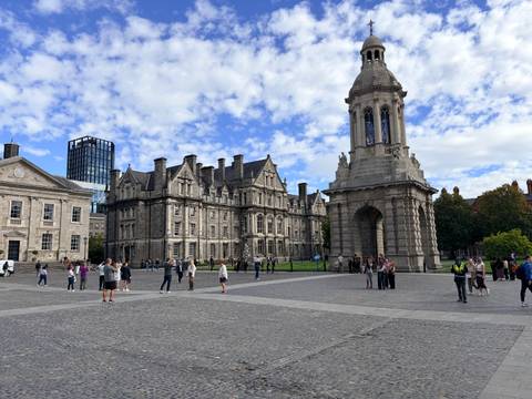 Courtyard scene at Trinity College Dublin with the Campanile tower and historic stone buildings under a blue-sky dotted with clouds.